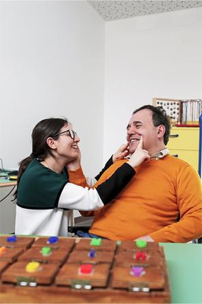 Alberto, un utente storico della Lega del Filo d'Oro, si scambia un sorriso con un'operatrice della stessa organizzazione. L'immagine cattura un momento di complicità e affetto