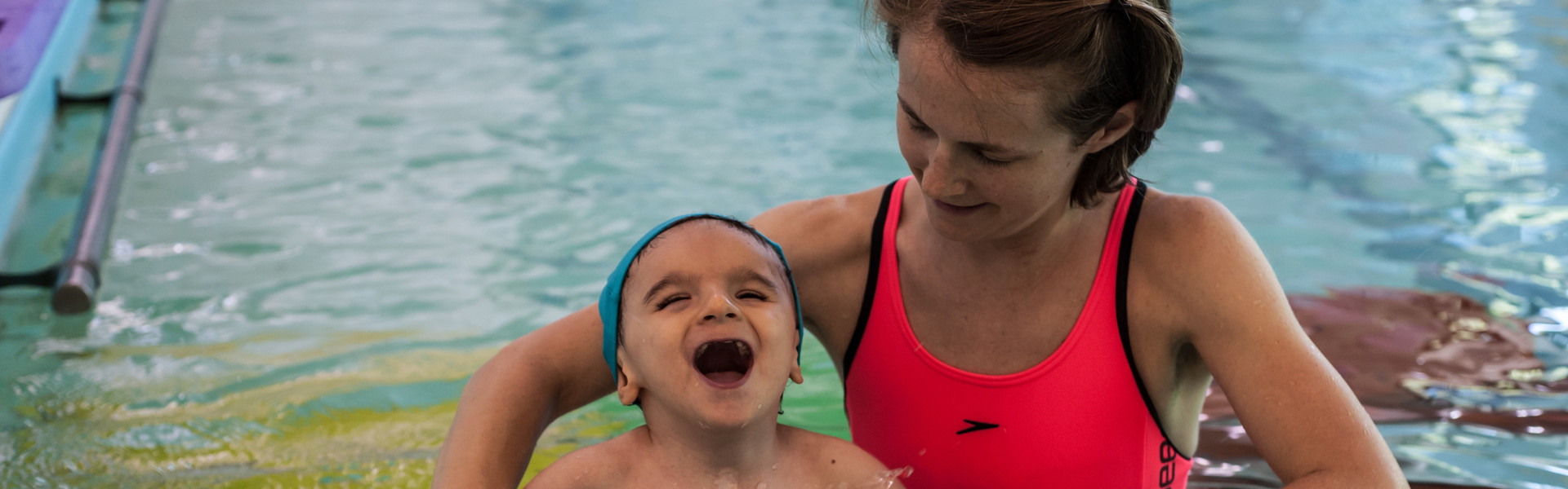 Idroterapia: la terapista della Lega del Filo d'Oro aiuta Nicolò a fare un esercizio in piscina con degli strumenti galleggianti e il bambino si diverte tantissimo