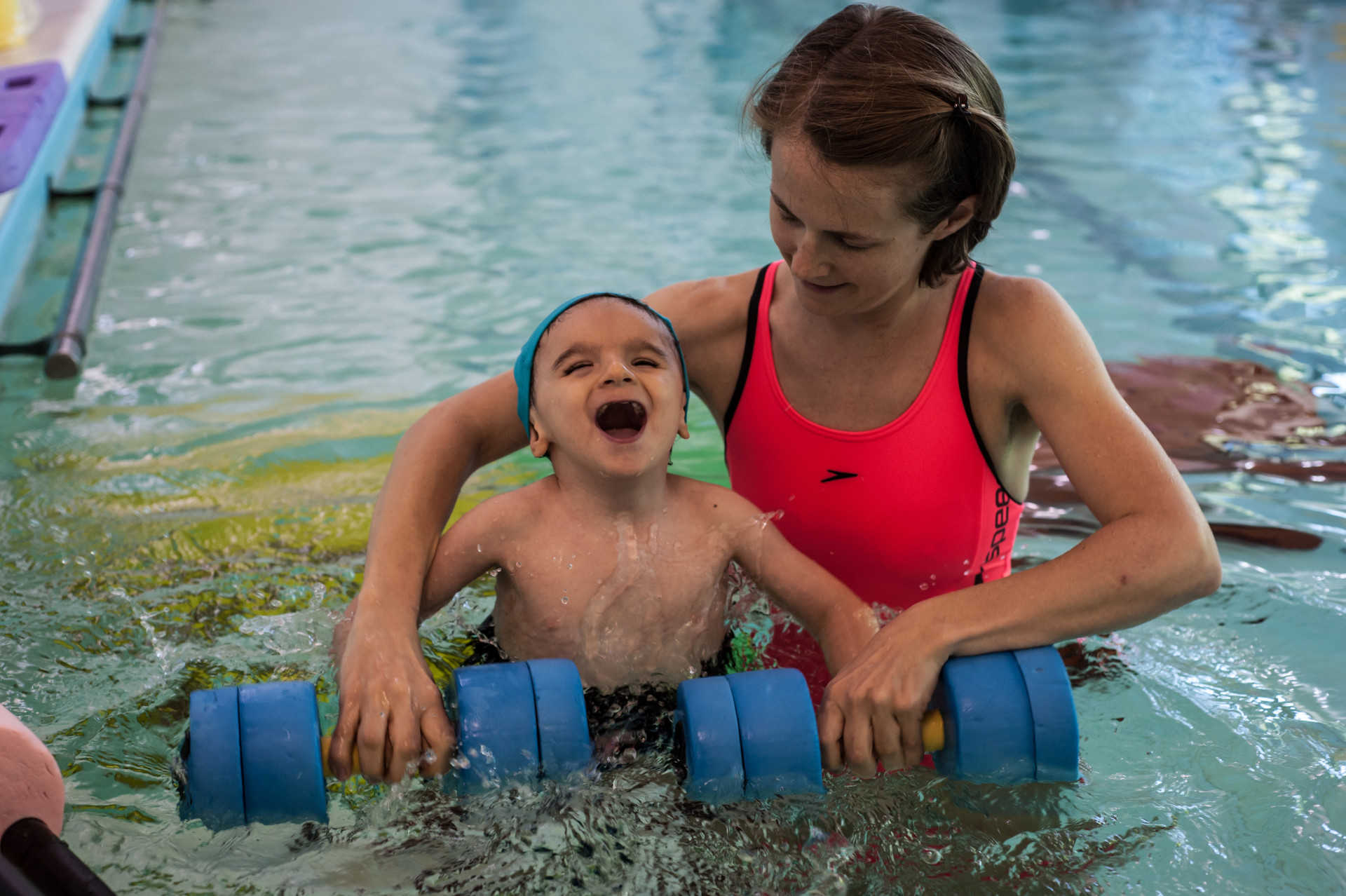 Idroterapia: la terapista della Lega del Filo d'Oro aiuta Nicolò a fare un esercizio in piscina con degli strumenti galleggianti e il bambino si diverte tantissimo