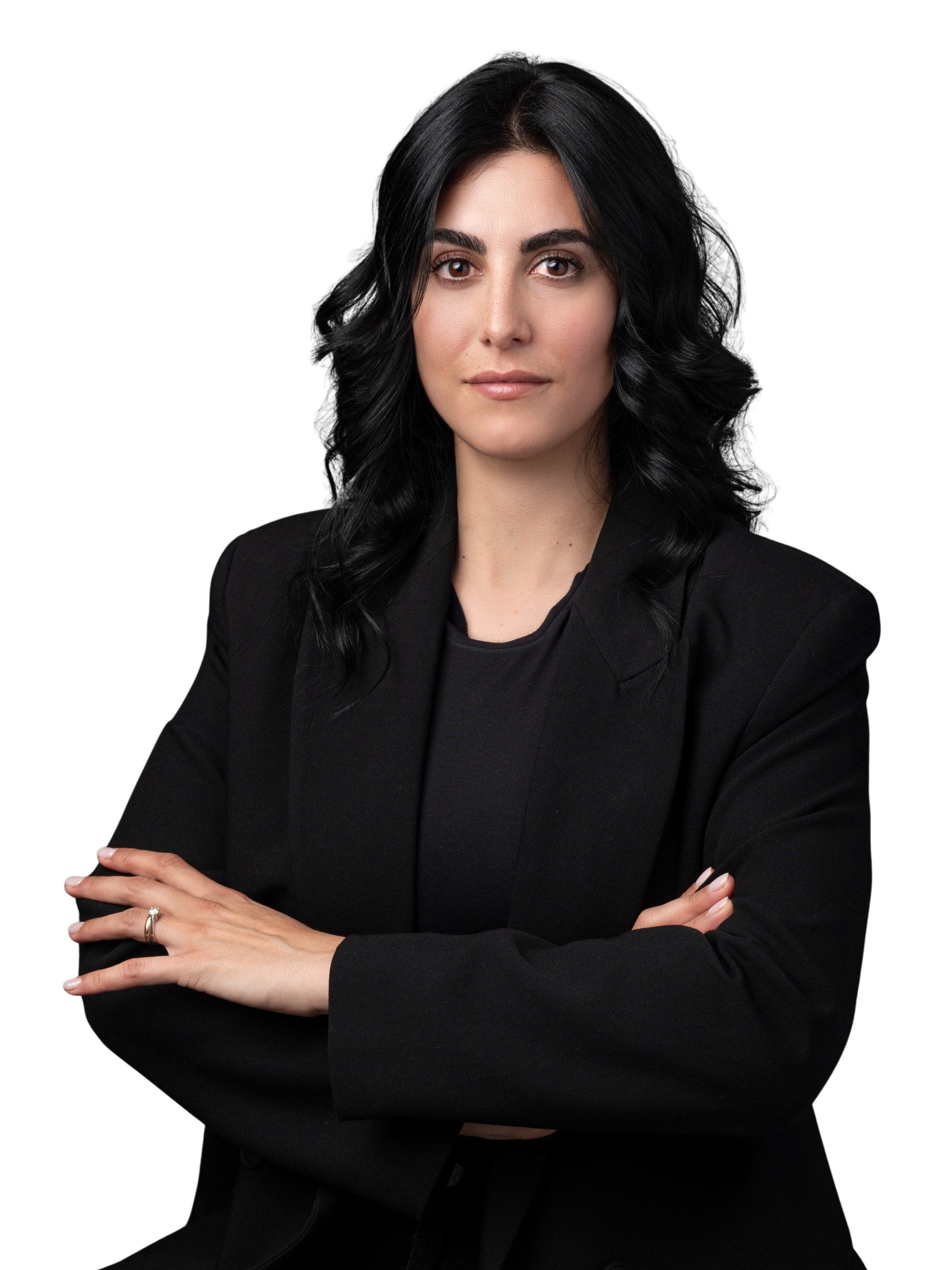 Donna in primo piano con occhi neri e capelli neri. Indossa una giacca nera. Ha le braccia incrociate. L'espressione è formale. 