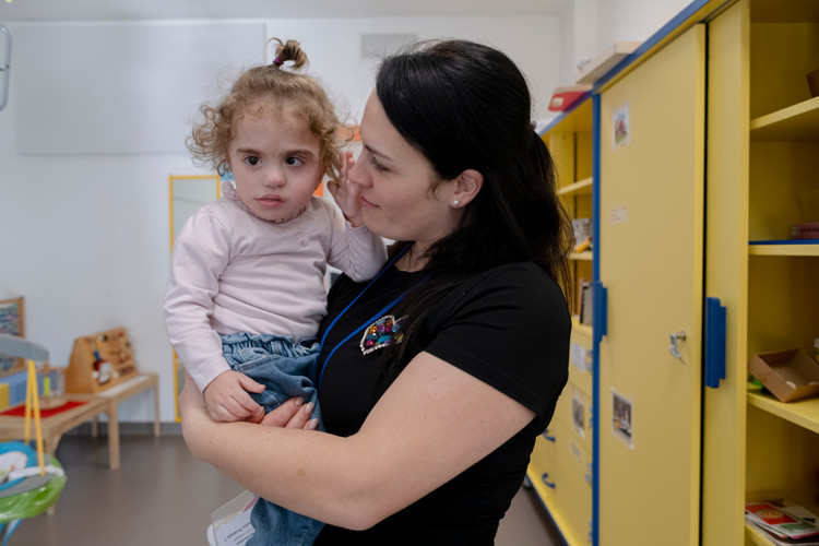 Benedetta viene tenuta in braccio dalla sua mamma, in un momento di affetto e tenerezza che trasmette amore e protezione.