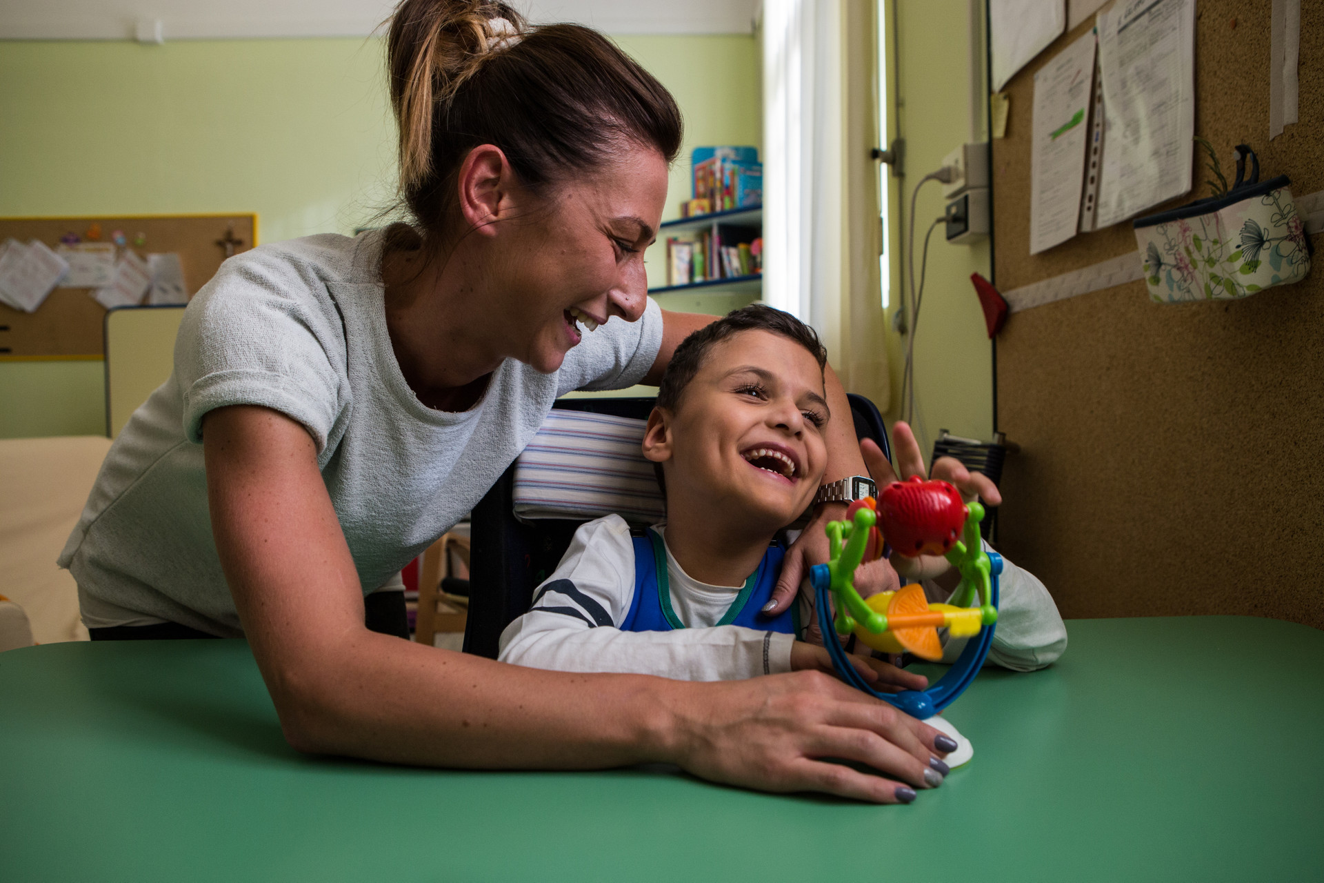 Francesco, un bambino ospite della Lega del Filo d'Oro, gioca con un giocattolo. Un'operatrice lo abbraccia e ride insieme a lui.