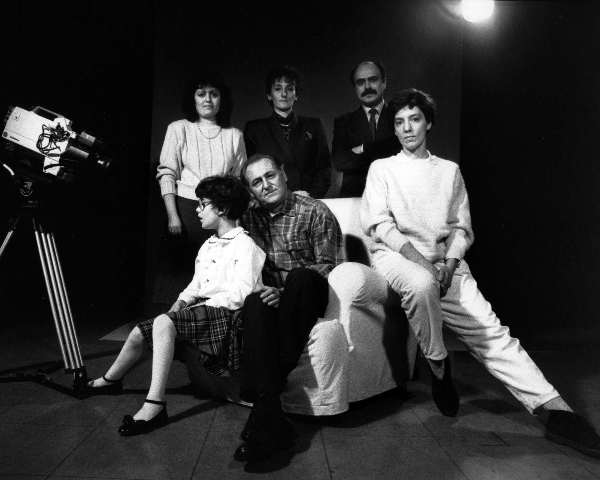 Foto in bianco e nero, scattata sul set di una campagna promozionale nel 1989. Si vede la macchina da presa e un gruppo di persone: tre sono sedute su una poltrona e sono una donna, Renzo Arbore e una bambina sordocieca; altre tre sono in piedi dietro di loro, si tratta di due donne e Rossano Bartoli.