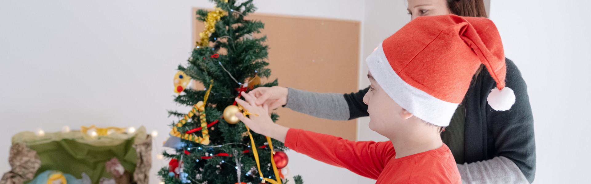 Un bimbo in età scolare con pluridisabilità psicosensoriale mentre accarezza la pallina di Natale accompagnato dalla sua educatrice