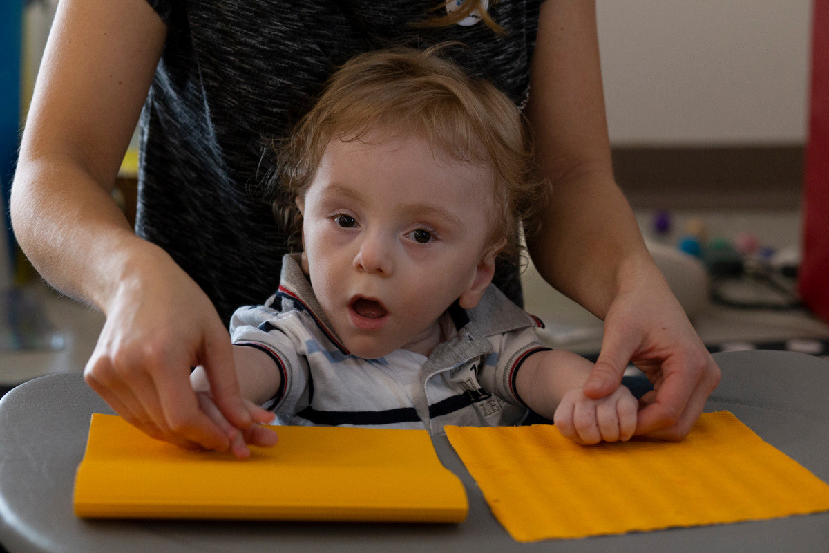 Il piccolo Gabriele, bambino utente del Centro di Osimo, esercita le sue capacità tattili con l'educatrice che gli guida le manine su superfici dalla consistenza diversa