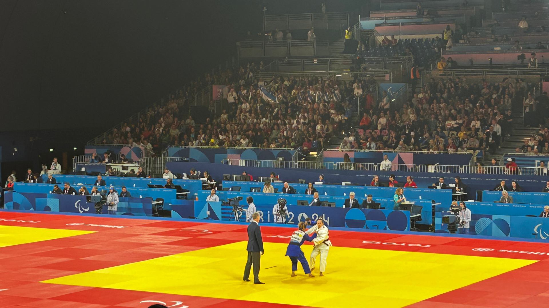 Panoramica dell’Arena del Palazzetto dello Sport di Parigi durante le Paralimpiadi 2024. Matilde Lauria, judoka sordocieca, è ritratta mentre combatte contro la sua avversaria. 