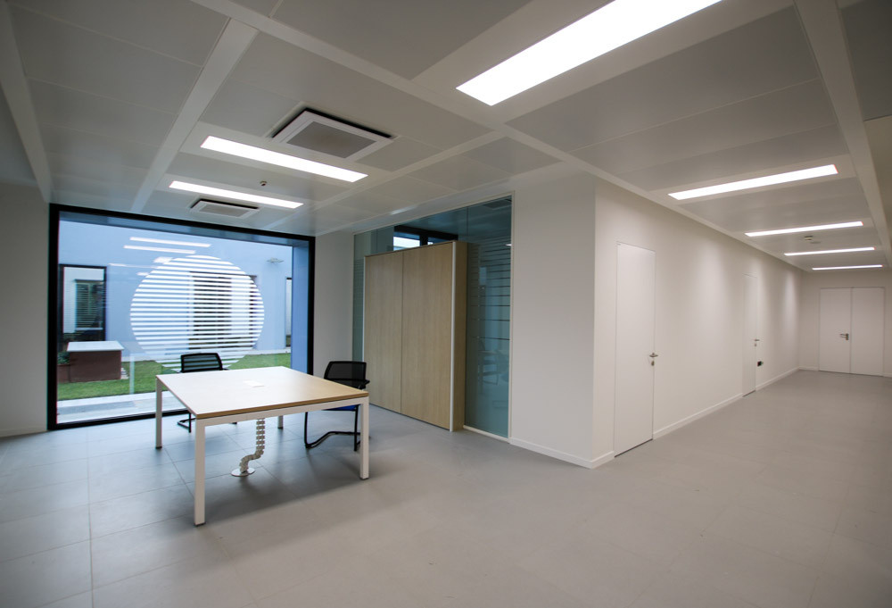 Un corridoio dell'edificio dedicato agli uffici nel primo lotto del Centro Nazionale. Un ambiente ampio con luce diffusa, in una rientranza del corridoio si vede un tavolo e, oltre una vestrata, uno dei giardini interni del Centro