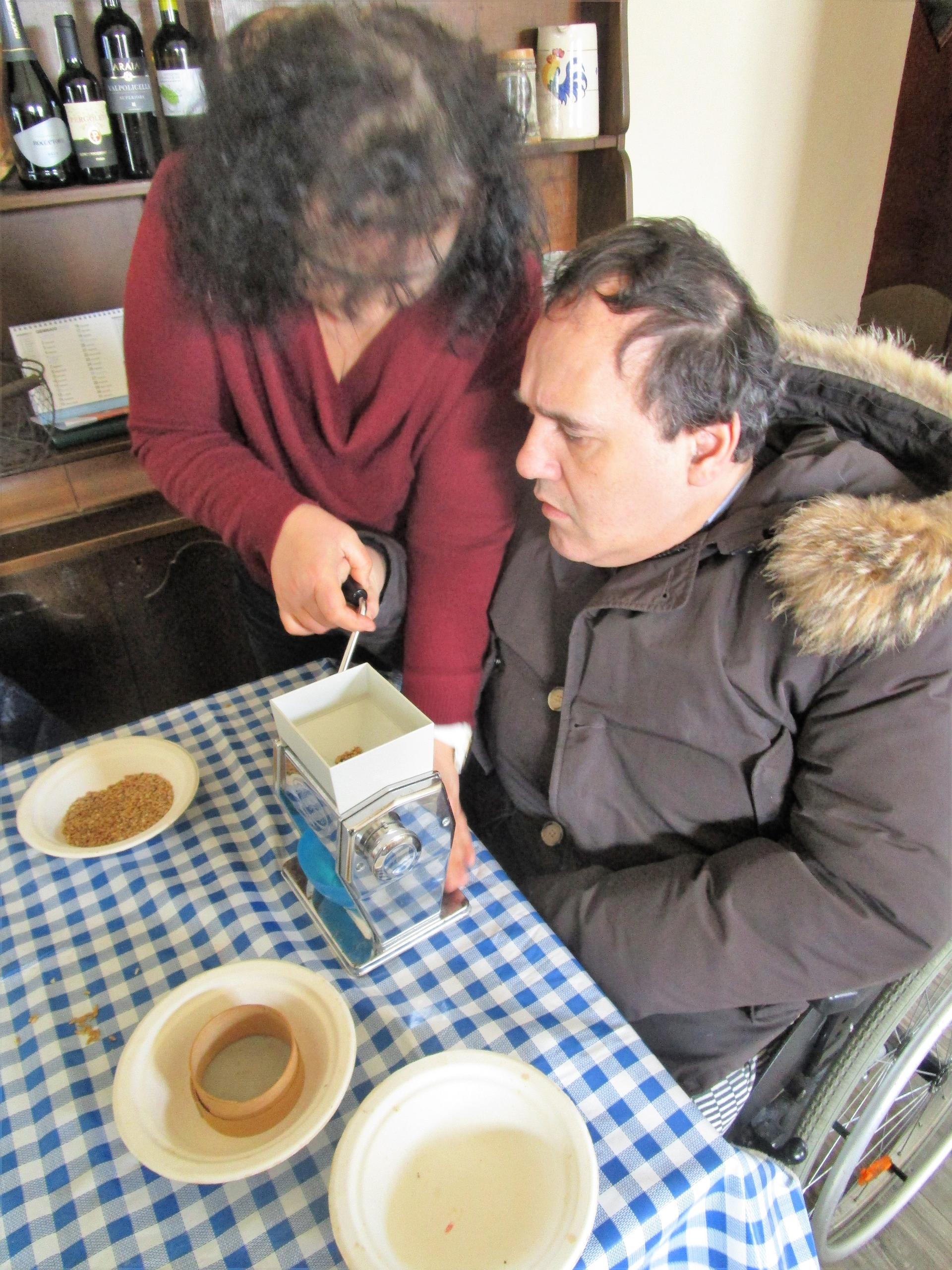 Alberto, un utente della Lega del Filo d'Oro è incuriosito dal macinino per macinare i cereali che viene azionato da una volontaria. Progetto "quanti cereali"