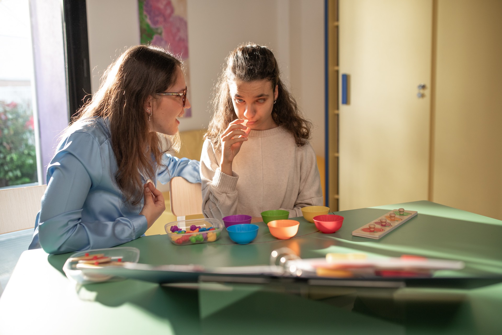 Aida è seduta davanti ad un tavolo pieno di forme e ciotole colorate, e lei, insieme alla sua educatrice, gioca con esse