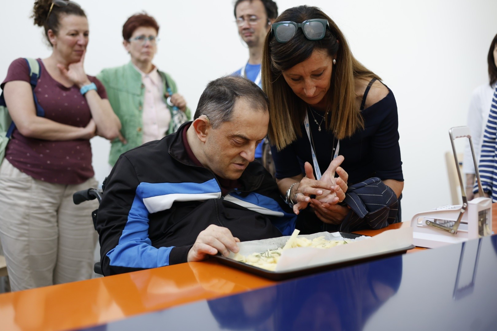 Un utente è in cucina didattica e sta preparando qualcosa da infornare. La sua educatrice è al suo fianco che gli prende la mano, e comunica con lui tramite il metodo Malossi