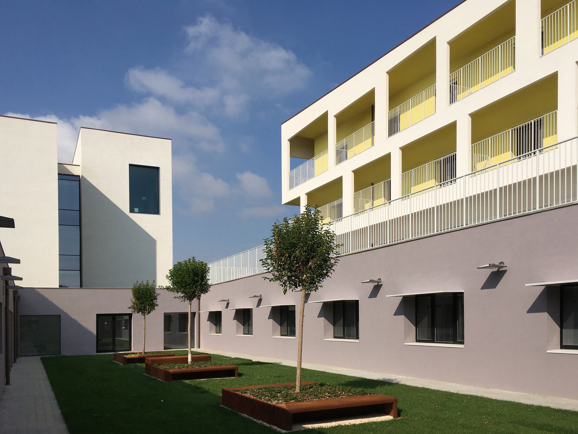 La foto inquadra uno dei giardini interni del primo lotto del Centro Nazionale, con alberi e panchine. Sopra di esso si elevano l'edificio degli uffici e quello dedicato al Centro Diagnostico