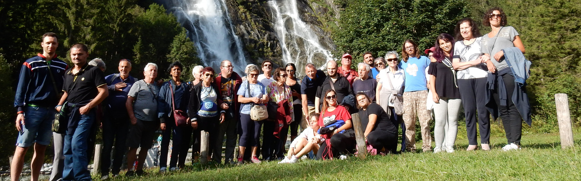 foto ricordo di un soggiorno estivo in montagna. Utenti, educatori e volontari posano in gruppo davanti a una cascata