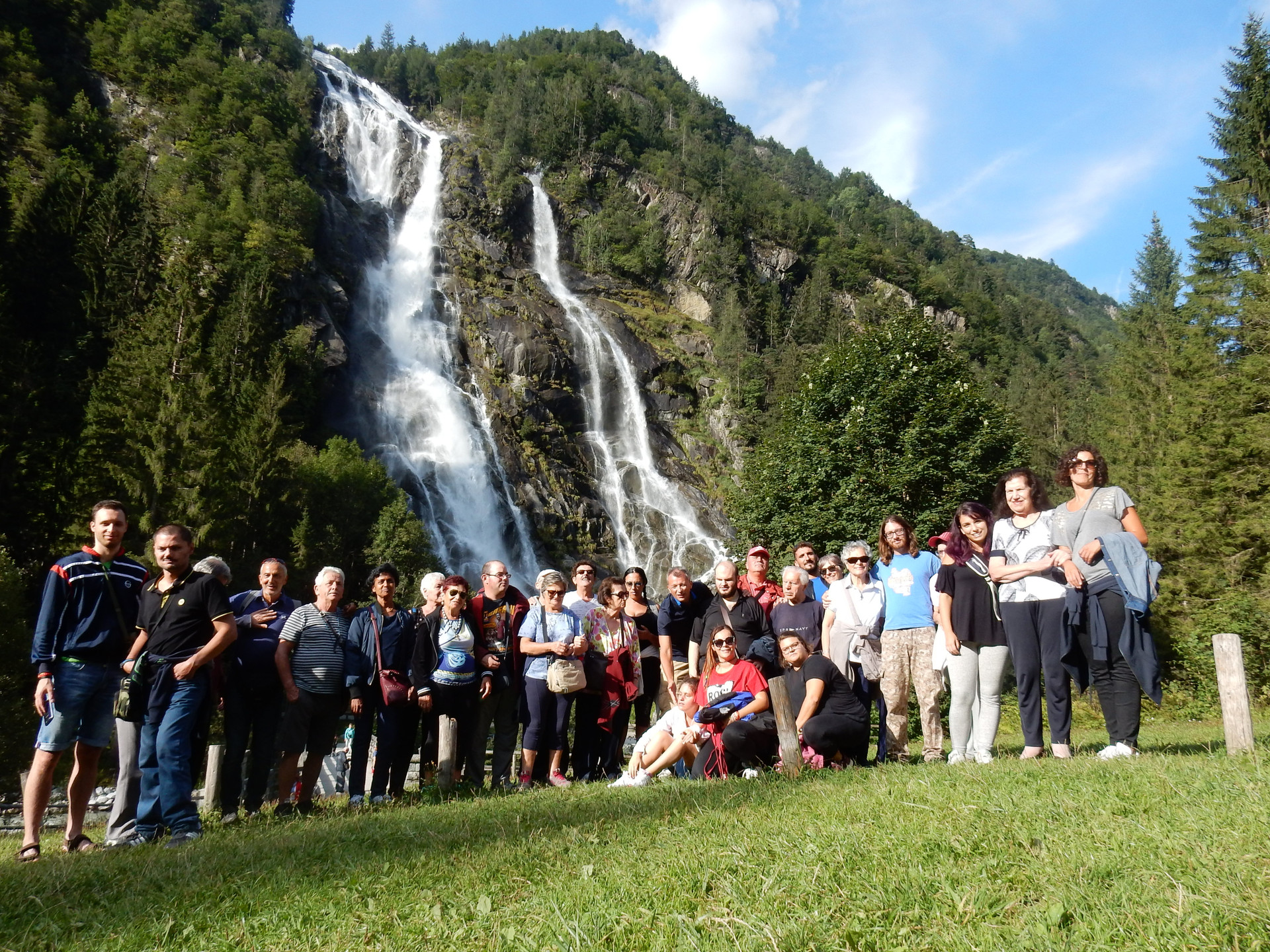 foto ricordo di un soggiorno estivo in montagna. Utenti, educatori e volontari posano in gruppo davanti a una cascata 