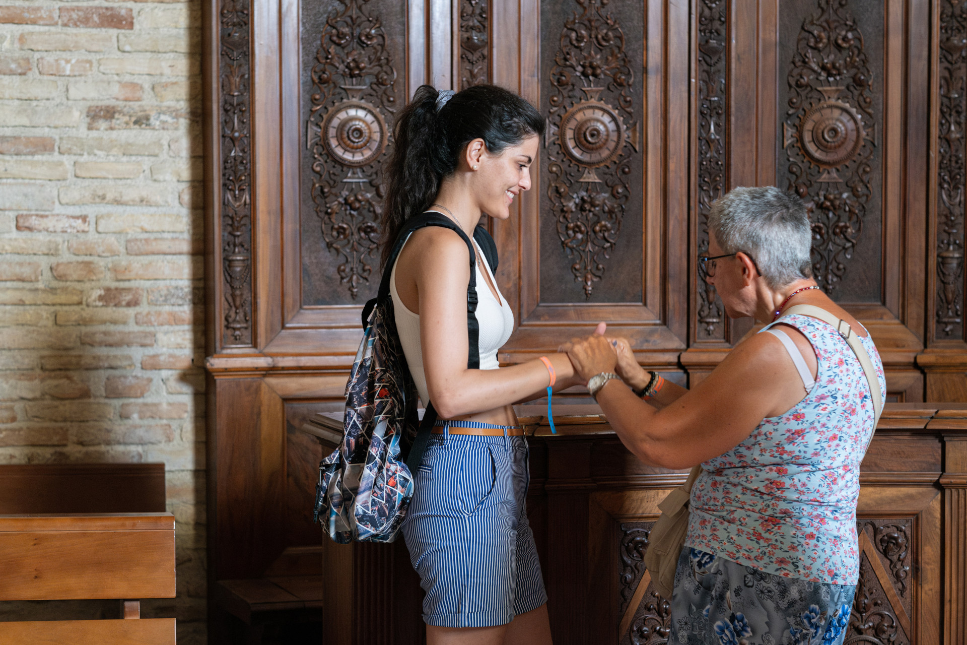 Una donna tiene le mani di un’educatrice in un luogo culturale, condividendo un momento di relazione profonda e scoperta, dove l’inclusione incontra la bellezza dell’arte.