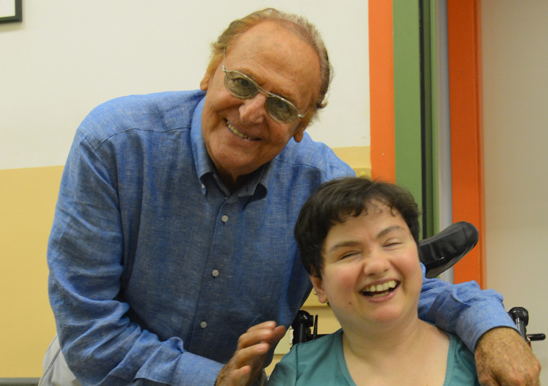 Foro in cui Renzo Arbore, storico testimonial della Lega del Filo d'Oro abbraccia Paola, una utente sordocieca che sorride entusiasta.