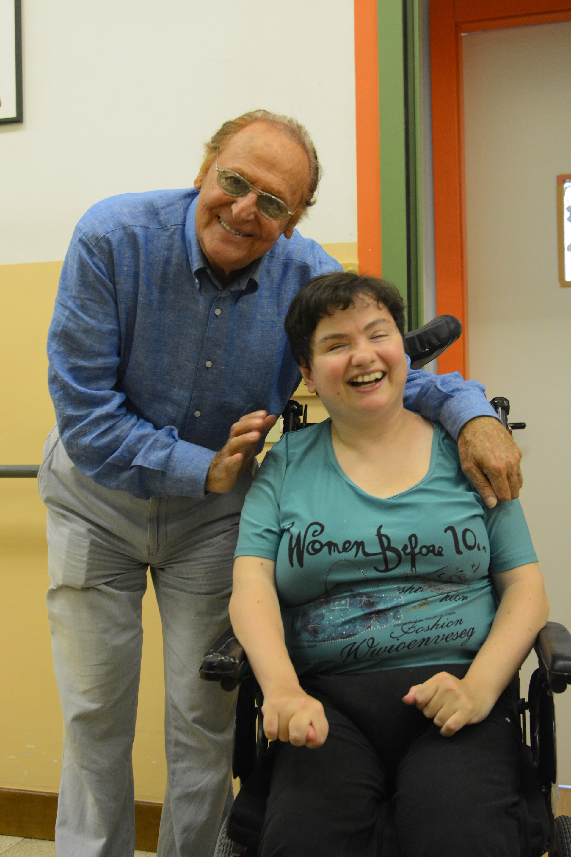 Foro in cui Renzo Arbore, storico testimonial della Lega del Filo d'Oro abbraccia Paola, una utente sordocieca che sorride entusiasta.