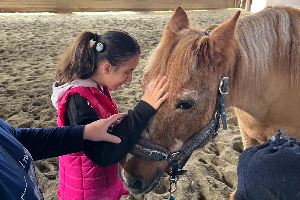 Utente della Lega del Filo d’Oro durante un’attività di pet therapy in un maneggio di Macerata. La bambina, sorridente e felice, aiutata da un operatore, accarezza con dolcezza il muso di un cavallo