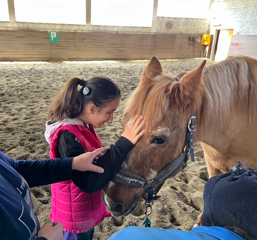 Utente della Lega del Filo d’Oro durante un’attività di pet therapy in un maneggio di Macerata. La bambina, sorridente e felice, aiutata da un operatore, accarezza con dolcezza il muso di un cavallo
