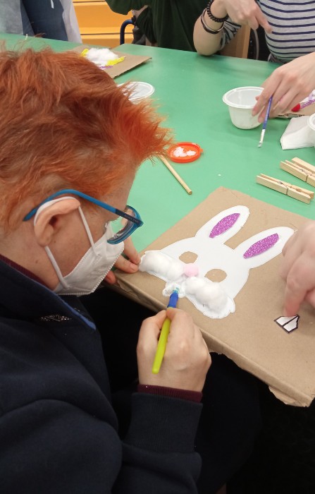 Un'utente adulta della sede di Novara svolge un laboratorio creativo colorando l'immagine di un coniglio su un supporto di cartone 