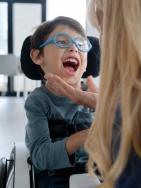 Nicola piccolo ospite in sedia a rotelle che ride per una carezza di un'educatrice