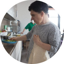 Stefania, ospite residenziale al Centro Nazionale di Osimo, regge in mano un tovagliolo con l'altra mano prende il piatto d'insalata dalla cucina