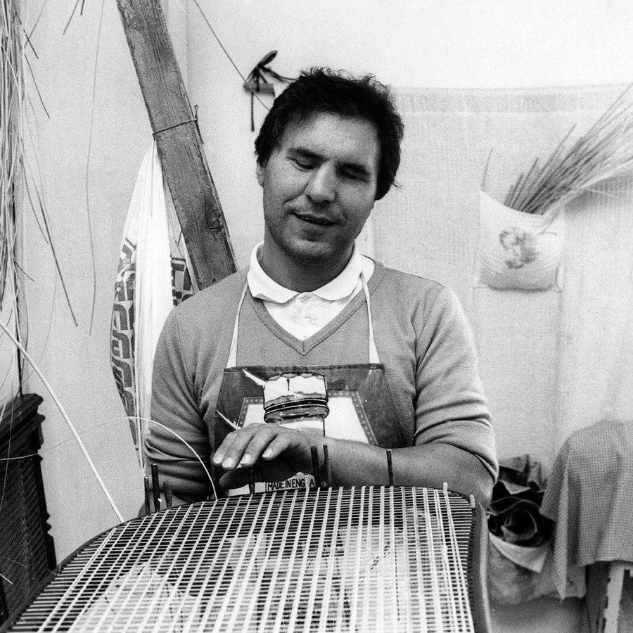 Immagine in bianco e nero degli anni '70. Un uomo sordocieco è fotograto mentre lavora ad un manufatto di vimini.