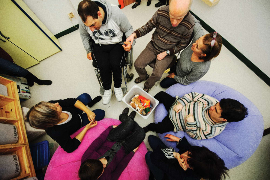Sette persone, sedute su segie e poltrone, sono fotografate dall'alto. Tra queste ci sono alcuni utenti e dei loro familiari.