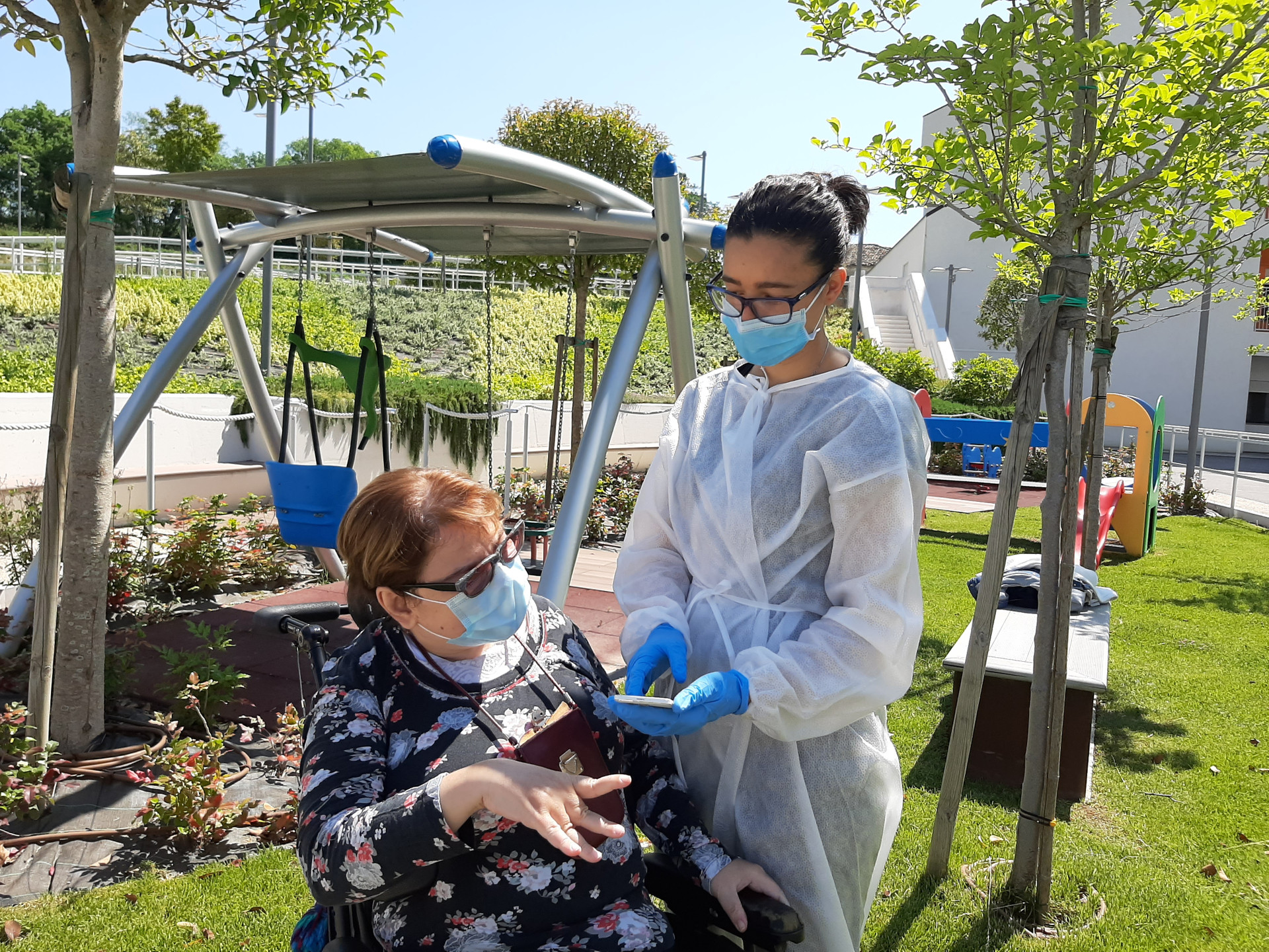 Paola, utente adulta del Centro di Osimo, nel giardino del Centro con un'educatrice che indossa il camice monouso, entrambe indossano le mascherine chirurgiche