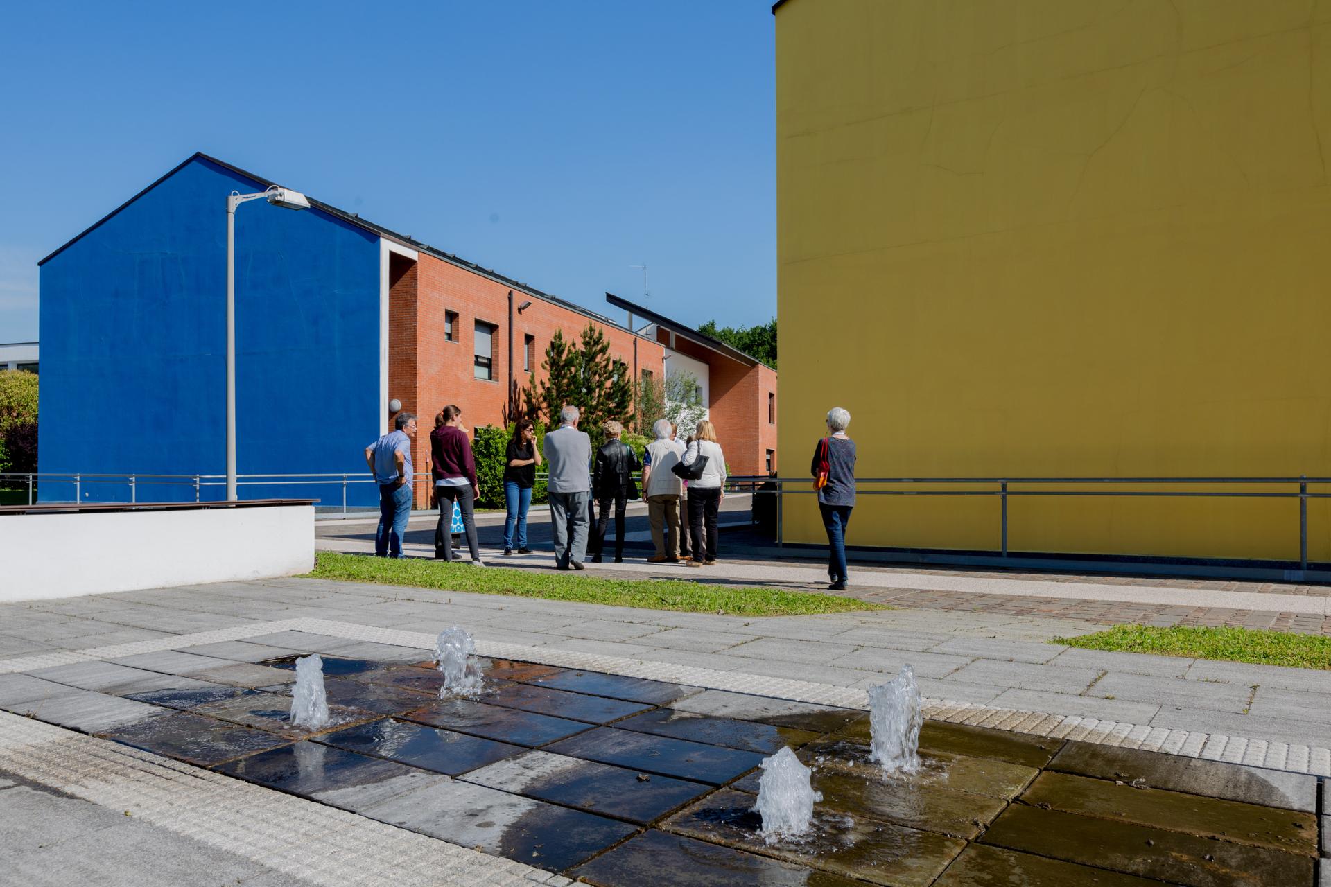 Giornata del Sostenitore - Centro di Lesmo con sostenitori in visita - sono visibili due delle tre palazzine residenziali e una fontanella che funge da segnale acustico per l'orientamento degli utenti.