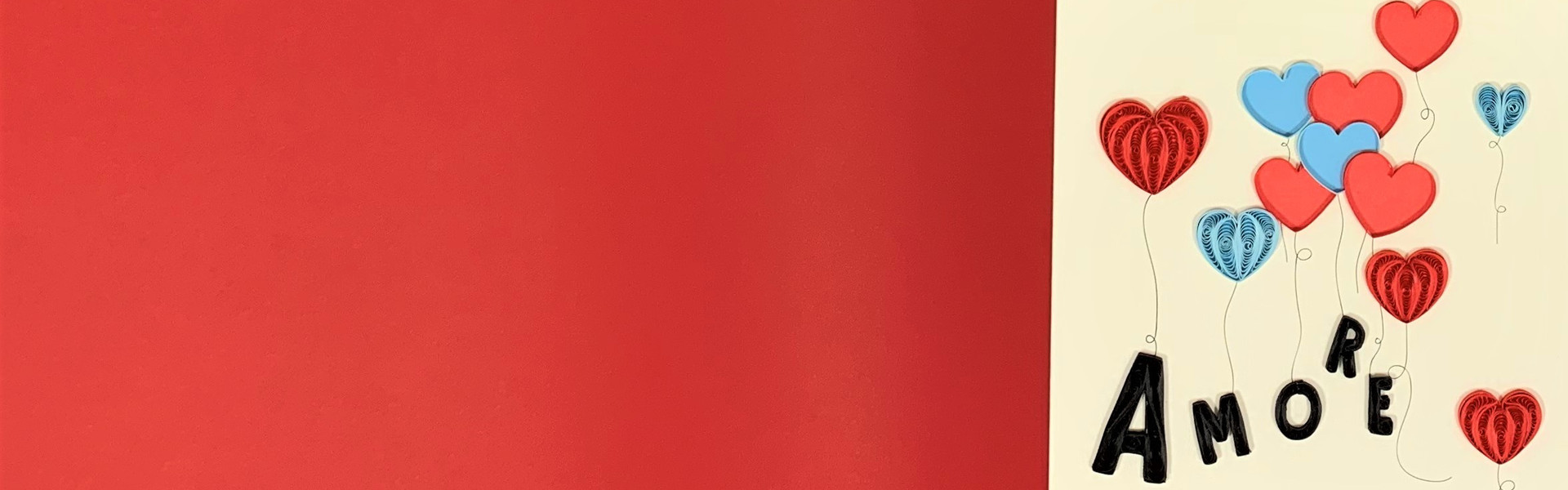 Composizione di regali solidali per San Valentino su sfondo rosso, inclusi portachiavi a forma di cuore, biglietto "Amore", bomboniera a forma di cuore, casetta in ceramica, pop grip e auricolari wireless. Perfetti per donare con amore e solidarietà.