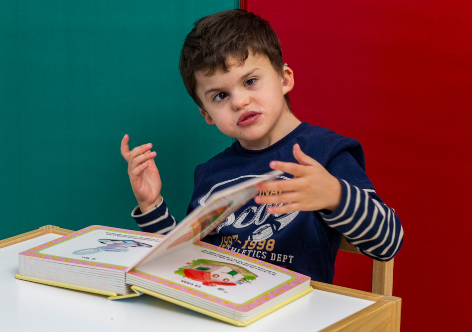 Agostino, un bambino della Lega del Filo d'Oro, sfoglia un libro di favole durante le sue attività riabilitative