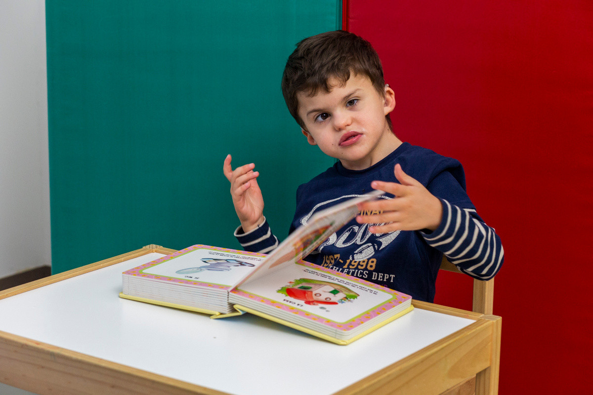 Agostino, un bambino della Lega del Filo d'Oro, sfoglia un libro di favole durante le sue attività riabilitative