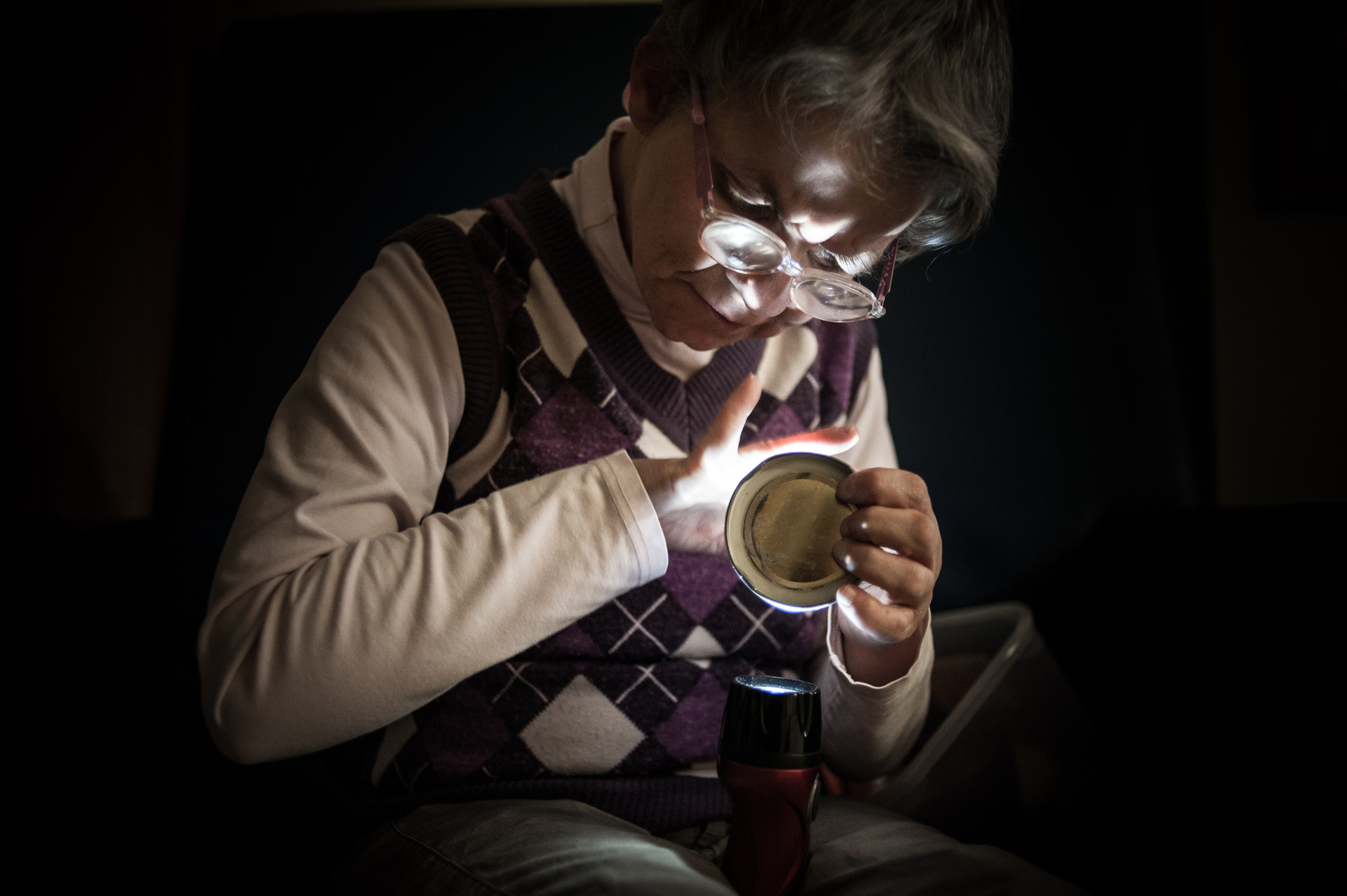 Scatto suggestivo tratto dallo spettacolo “Il Condominio Sogni” della compagnia inclusiva “Il Cantiere dei Sogni”. In primo piano, un utente della Lega del Filo d'Oro: il suo volto emerge dal buio grazie alla luce di una torcia.