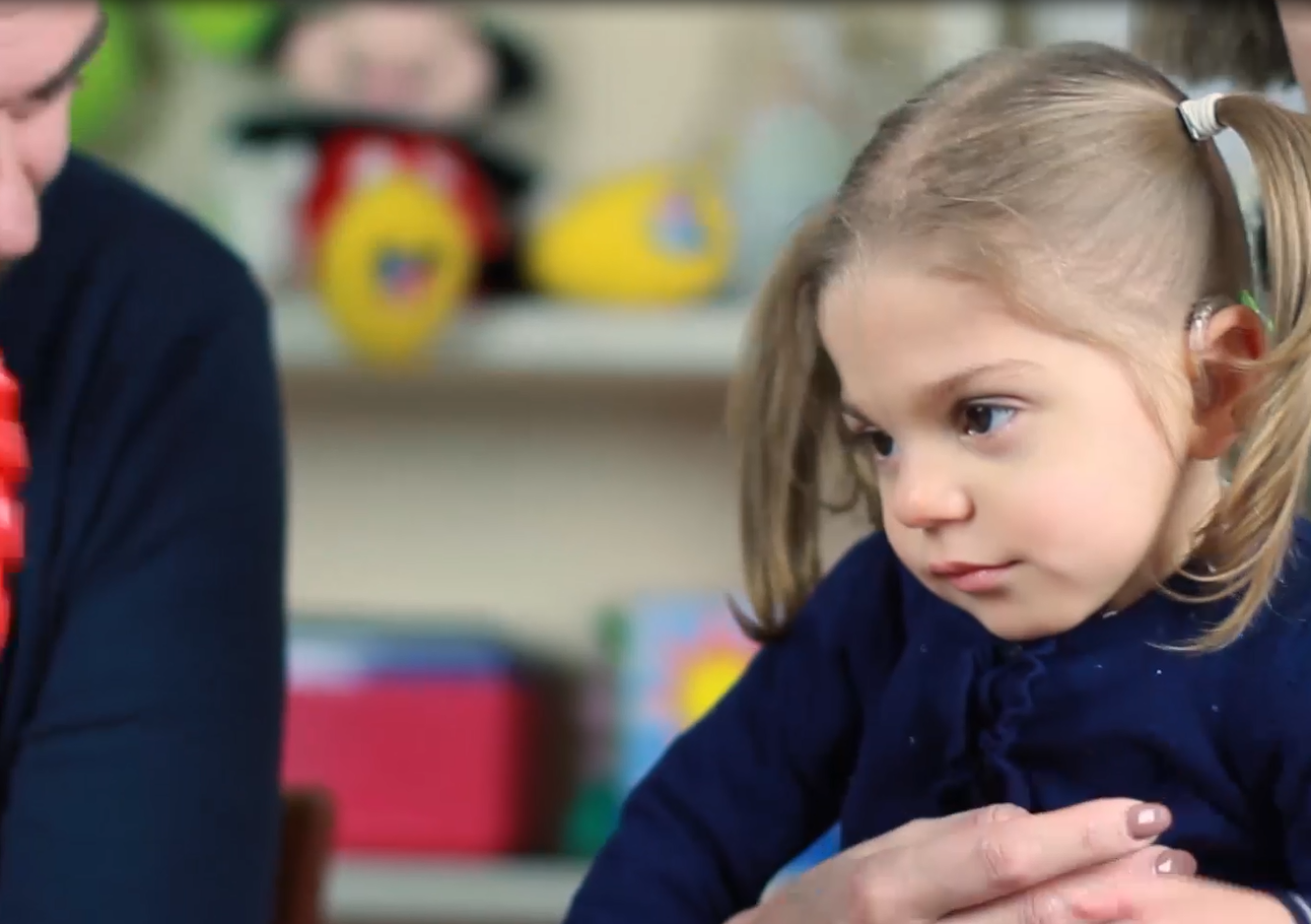 Sveva, bambina di 4 anni con sindrome di Charge, guarda un giocattolo colorato che le sta mostrando il suo papà