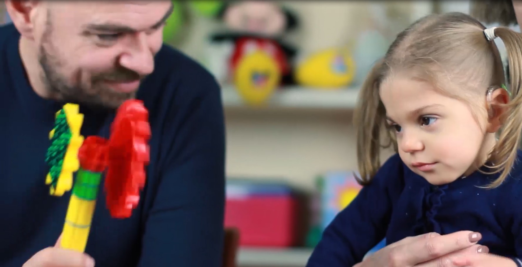 Sveva, bambina di 4 anni con sindrome di Charge, guarda un giocattolo colorato che le sta mostrando il suo papà
