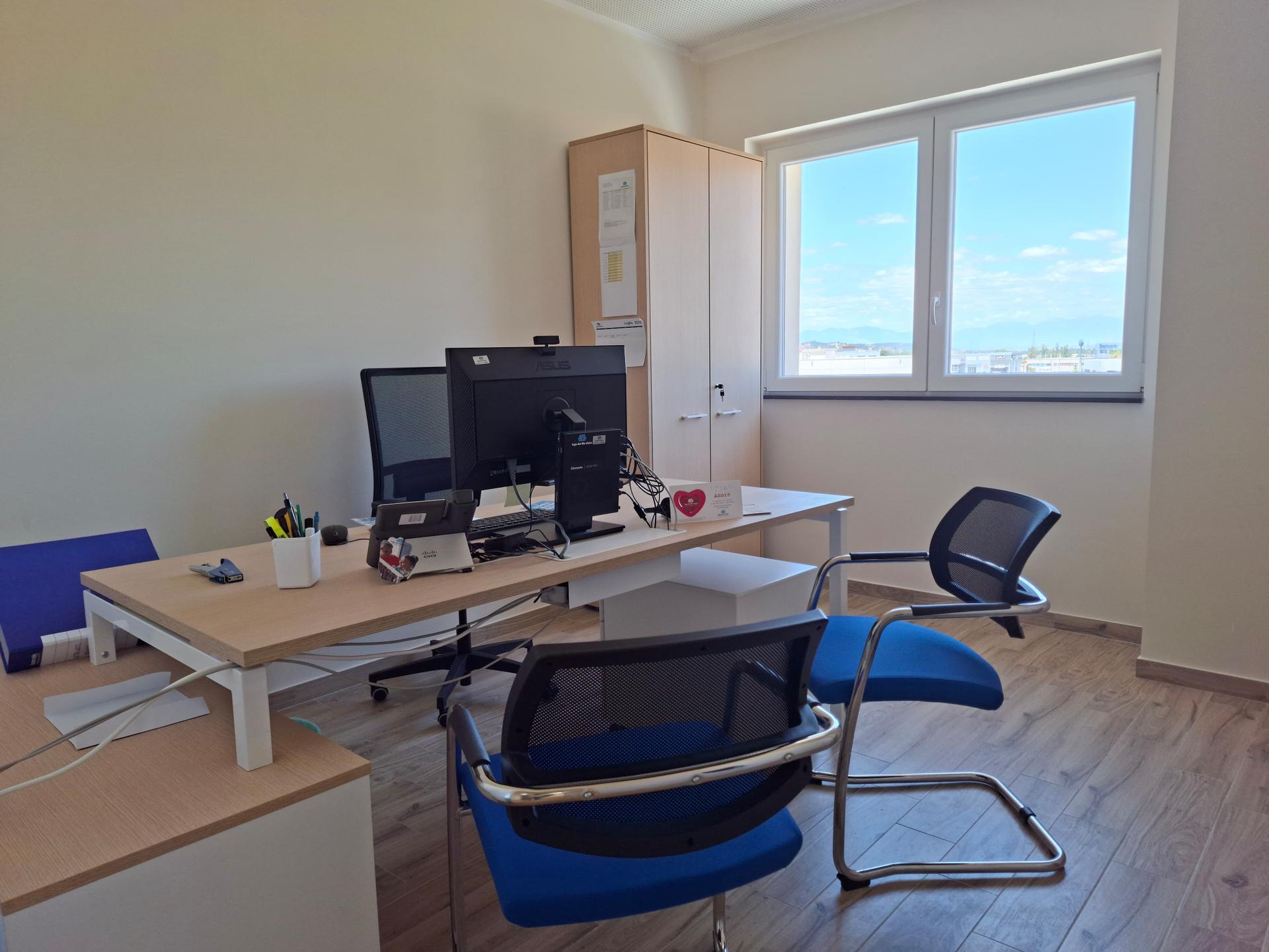All'interno dell'ufficio della sede, c'è una scrivania con un pc, delle sedie blu, un armadietto e una finestra con panorama