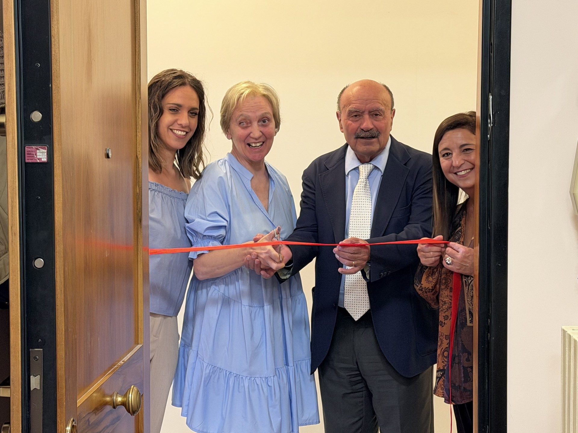 Momento inaugurale del nuovo progetto di vita indipendente attivato nel Comune di Osimo. Quattro persone partecipano al taglio del nastro all'ingresso dell'appartamento. Da sinistra l'assistente sociale della Lega del Filo d'Oro, la beneficiaria del progetto di vita indipendente, il Presidente della Fondazione e l'operatrice territoriale del Servizio Territoriale di Osimo dell'Ente