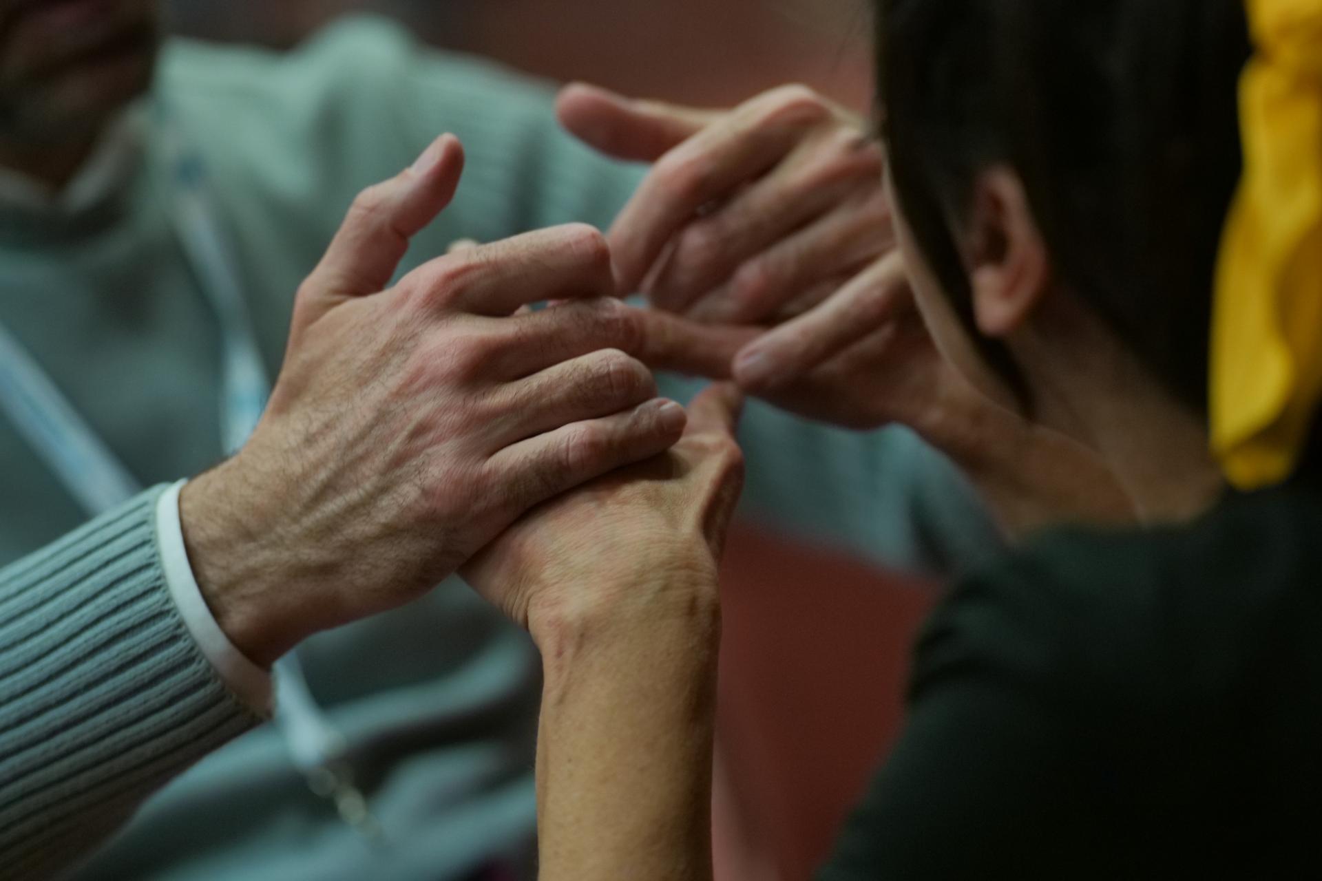 Un utente della Lega del Filo d’Oro comunica con una donna attraverso la LIST. L’immagine, sfocata sulle figure, mette a fuoco solo le mani che si toccano.