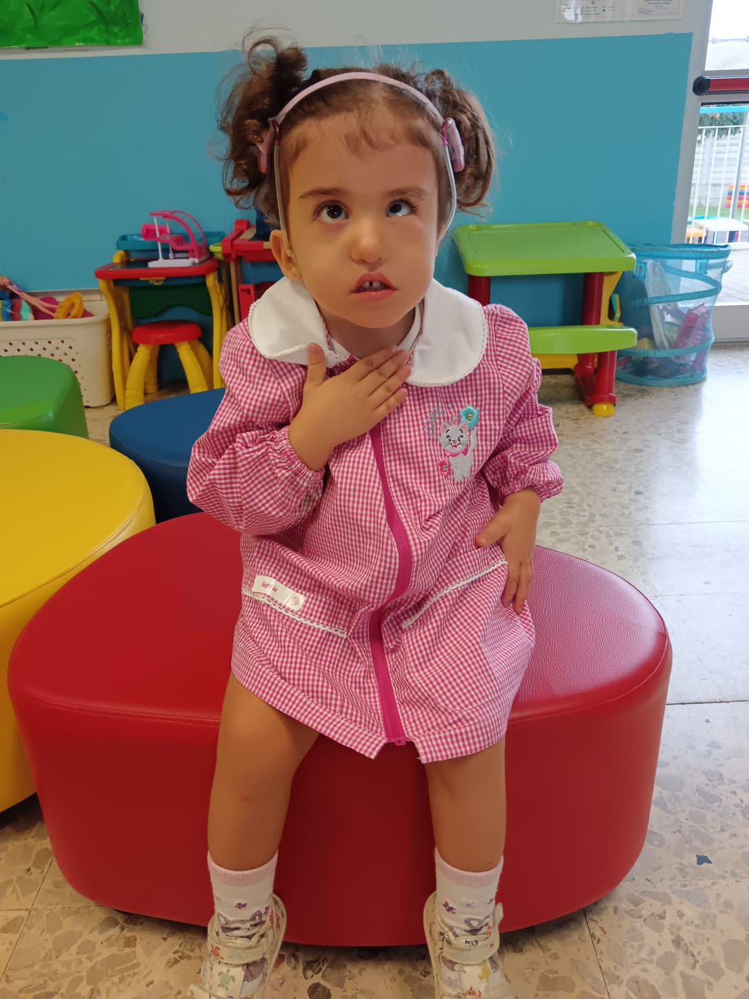 Sophie, con il suo grembiulino rosa, seduta sopra un pouffe rosso, sta comunicando con chi sta scattando la foto