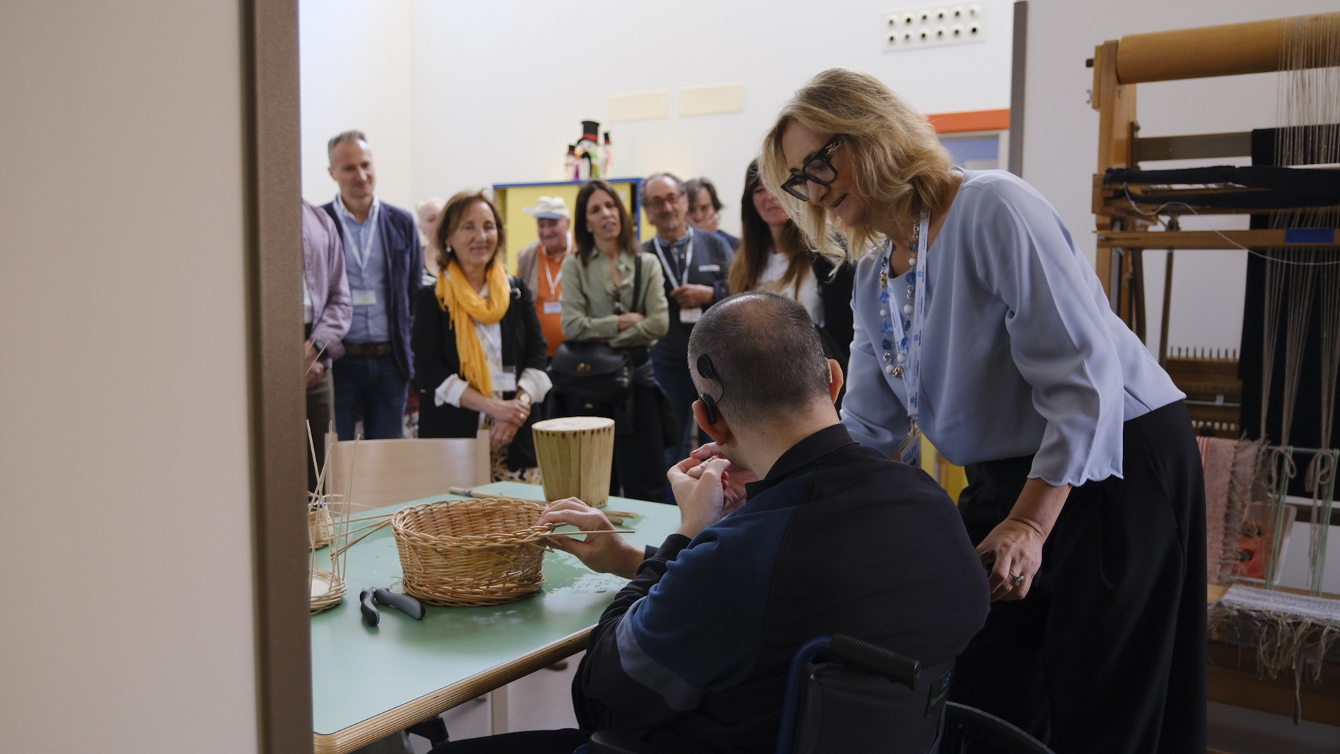 Nicoletta Marconi, psicologa del Centro Nazionale, è in un laboratorio didattico con un utente impegnato nella realizzazione di un cestino, osservati da alcuni sostenitori.