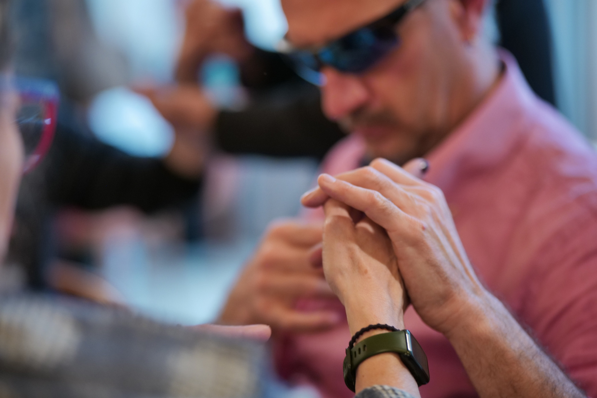 Due mani si toccano utilizzando la LIS Tattile, con un uomo con sordocecità e occhiali da sole sullo sfondo.