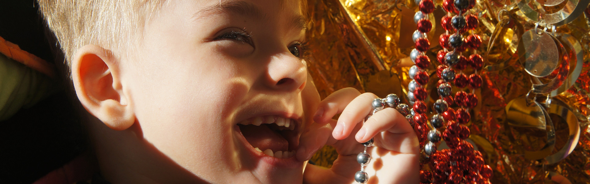 Primo piano di Edoardo, bambino di 3 anni ospite del Centro di Osimo, che ride giocando con delle catenelle rosse e oro durante una seduta di stimolazione sensoriale