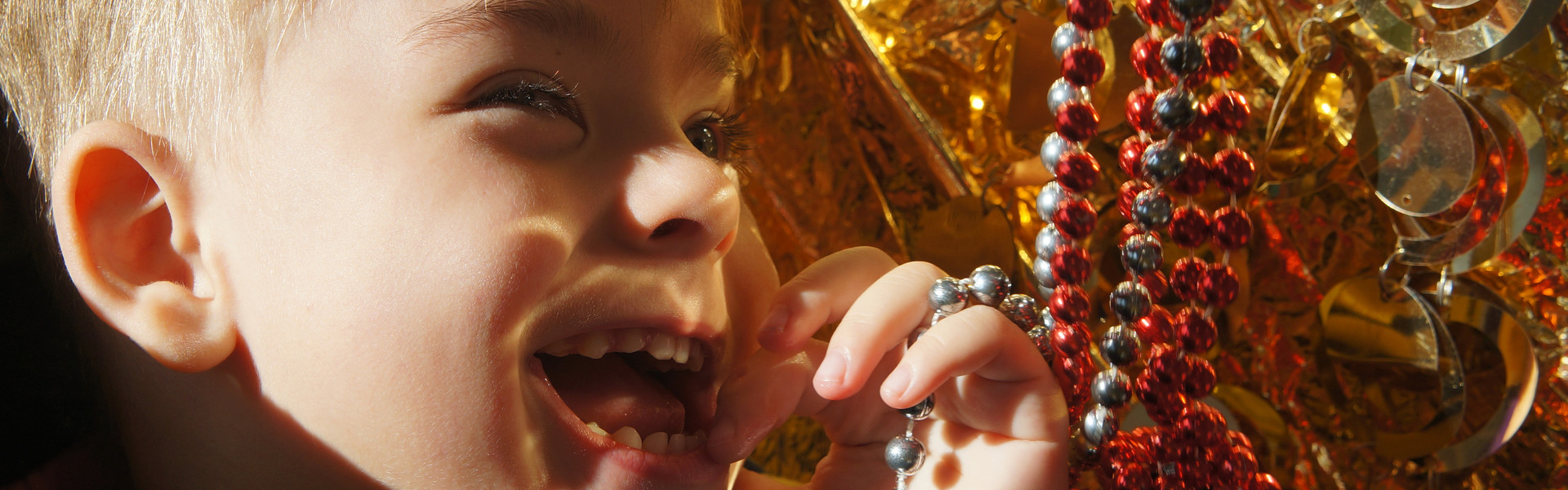 Primo piano di Edoardo, bambino di 3 anni ospite del Centro di Osimo, che ride giocando con delle catenelle rosse e oro durante una seduta di stimolazione sensoriale