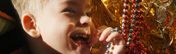 Primo piano di Edoardo, bambino di 3 anni ospite del Centro di Osimo, che ride giocando con delle catenelle rosse e oro durante una seduta di stimolazione sensoriale