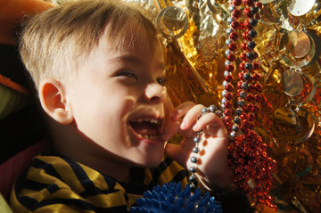 Primo piano di Edoardo, bambino di 3 anni ospite del Centro di Osimo, che ride giocando con delle catenelle rosse e oro durante una seduta di stimolazione sensoriale