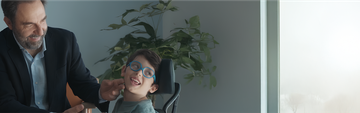 Ritratto di Neri Marcorè e Nicola, un bambino con problemi motori e alla vista, sorridenti insieme. Un’immagine di empatia, inclusione e positività che racconta un incontro speciale.