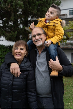 Leonardo, un bambino utente della Lega del Filo d'Oro, è a cavallo delle spalle di suo nonno in una foto scattata all'aperto dove è presente anche sua nonna, i tre sorridono a favore di camera