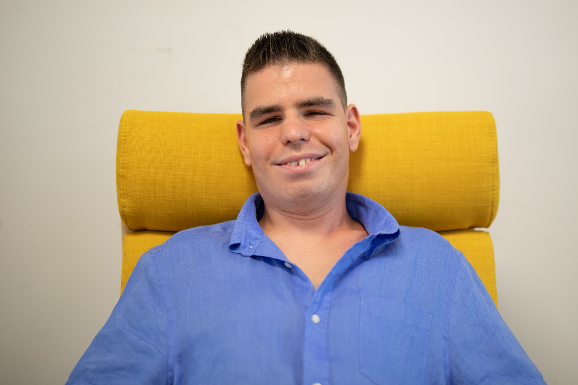 Benedetto sorridente è seduto su una comoda poltrona gialla