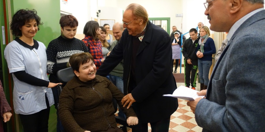 Il saluto di Renzo Arbore, testimonial della Fondazione, a Paola, ospite residenziale del Centro Nazionale di Osimo. Nella foto compare anche il Presidente Rossano Bartoli e altri ospiti ed educatori della Lega del Filo d'Oro. La foto è stata scattata nel vecchio centro di Osimo, S. Stefano
