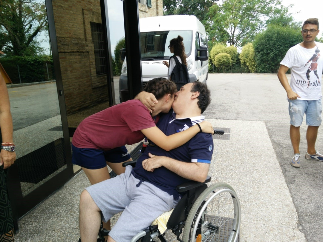 Alberto, utente adulto del Centro di Osimo, si trova fuori dalla sede storica, scambia un abbraccio con una volontaria scout e le schiocca un bacio sulla guancia
